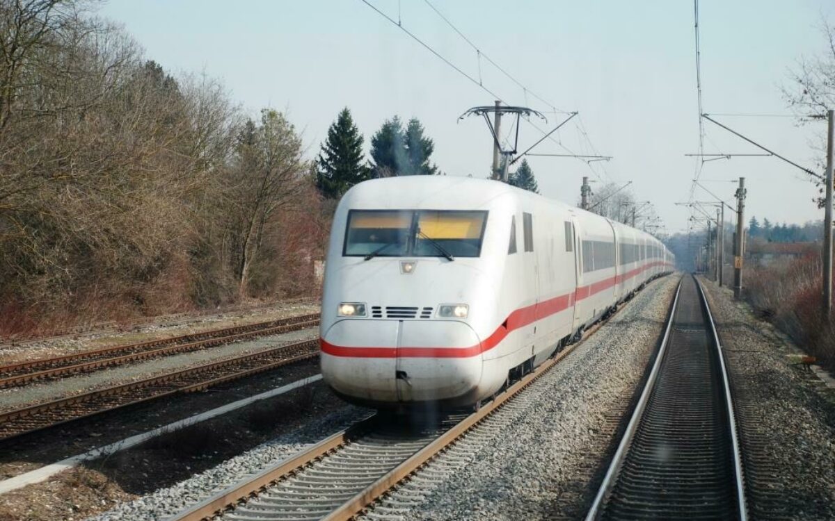 Ein weiß-roter ICE-Zug fährt Gleise entlang, links und rechts sind Bäume ohne Blätter Ein weiß-roter ICE-Zug fährt Gleise entlang, links und rechts sind Bäume ohne Blätter